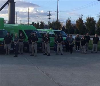 15 people standing outside in front of green trucks