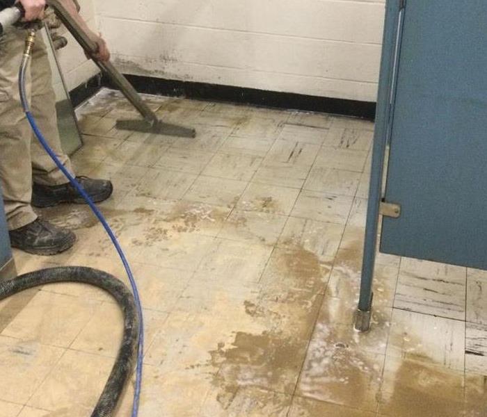 A business bathroom stall with dried mud on the floor and a SERVPRO technician cleaning it.
