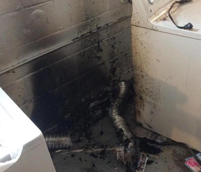 Dryer pulled away from wall with soot debris on it.  The wall is fire damaged and the dryer vent is destroyed on the floor