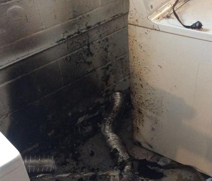 A dryer against block wall with burned marks on the dryer and wall.  Dryer vent on the floor with damage.