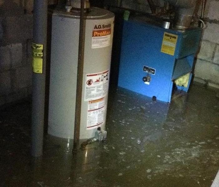 A basement filled with dirty water and furnace and hot water tank partially submerged under the water